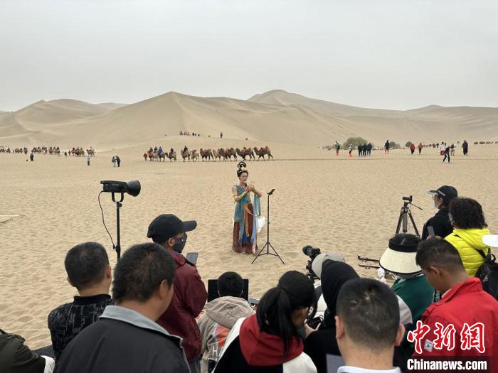 圖為2023年4月底，敦煌大漠“逐舞者”奧楠在鳴沙山月牙泉景區(qū)視頻直播，吸引游人圍觀?！●T志軍 攝